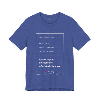 A heather blue crewneck t-shirt with a white graphic print containing care instructions and a quote by 'n+1 a shape' on the front, displayed against a solid white background.