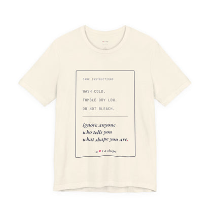 An off-white short-sleeve crewneck t-shirt with a printed care instructions graphic on the front, featuring text that reads 'WASH COLD. TUMBLE DRY LOW.