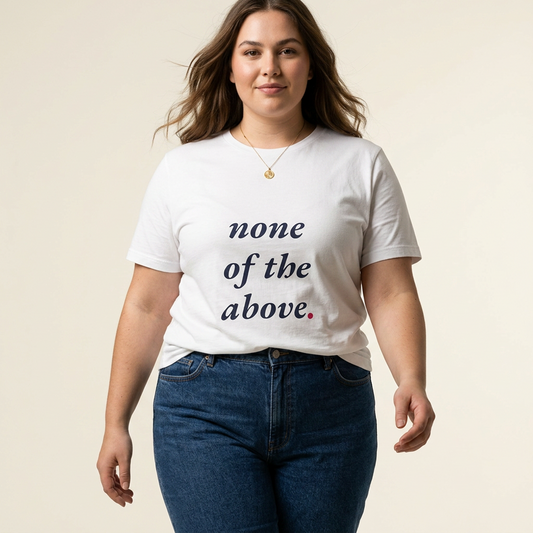 A woman modeling "not a shape" white graphic t-shirt with the text 'none of the above.' printed in dark navy and pink, paired with dark blue jeans against a solid light beige background.