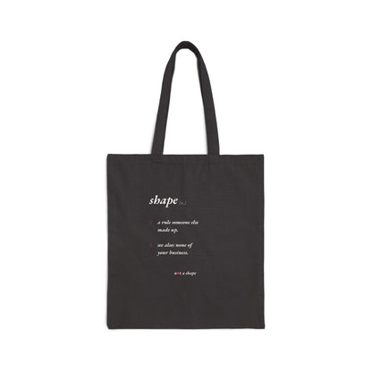 A black canvas tote bag with two black shoulder straps, featuring a white printed dictionary-style definition of the word 'shape' on the front. The bag is photographed against a clean, solid white background.